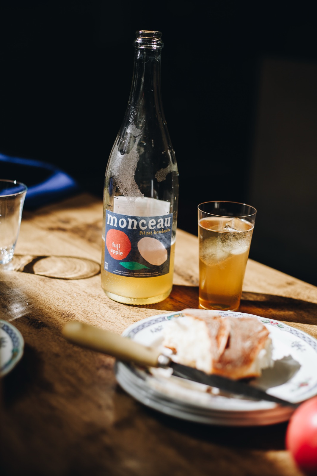 A bottle of Monceau and a glass on a wooden table beside a plate of cheese