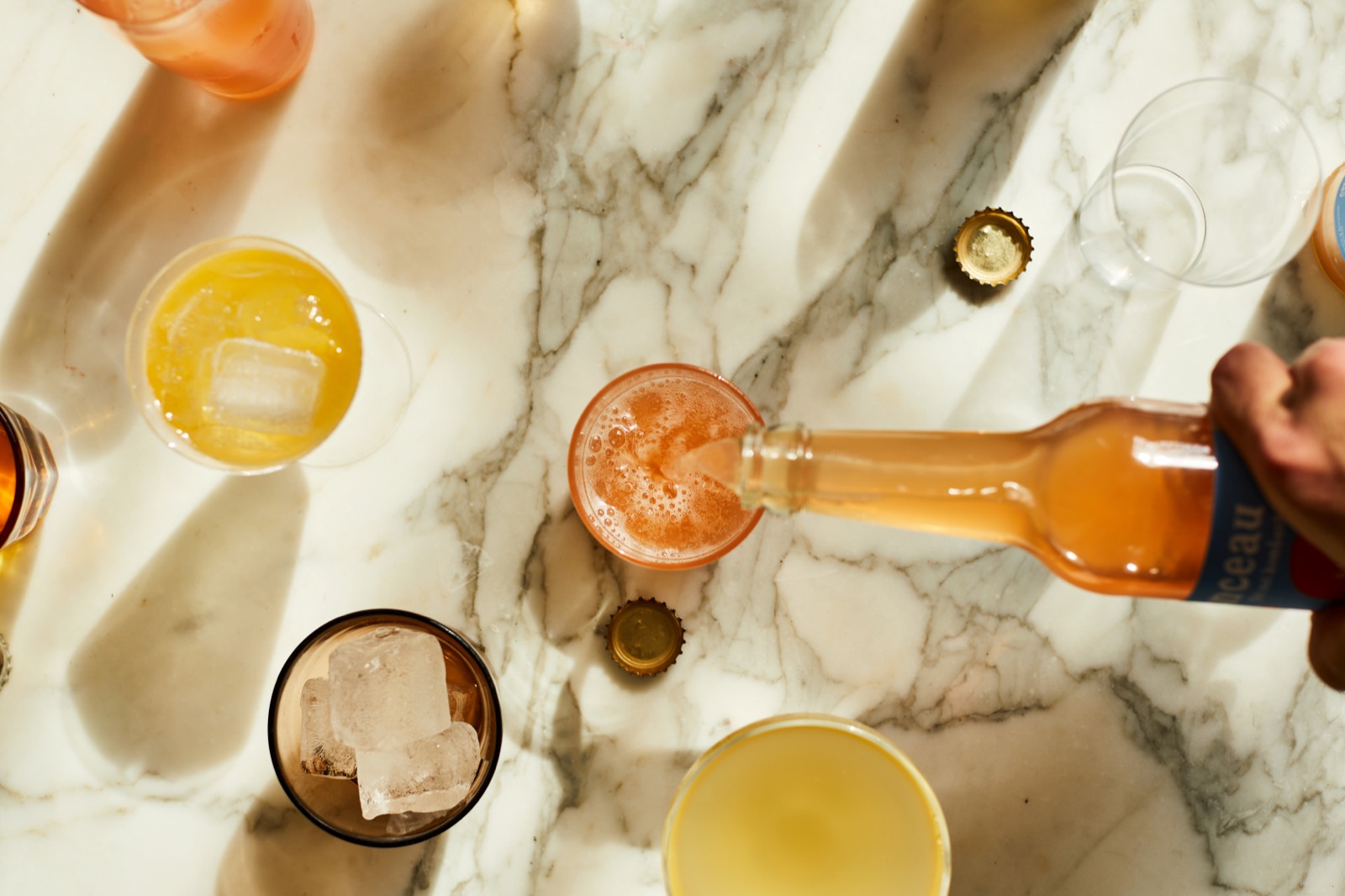 Kombucha being poured into a glass from above, on a marble table with ice