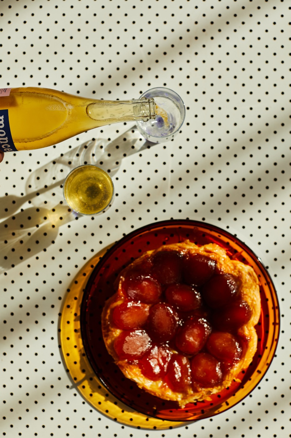 A bottle of kombucha being poured beside a plum tart